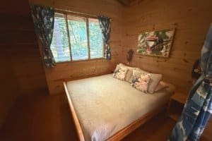 Intimate bedroom with wooden walls, large window, and tropical decor in Dominical.