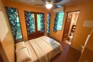 Comfortable bedroom with tropical curtains, balcony, and nearby bathroom in Dominical.
