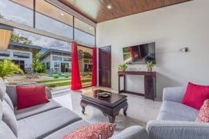 Bright living room with gray sofas, red cushions, glass doors, and pool view.