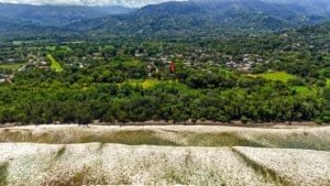 Aerial view of Dominical coastline with beach, greenery and distant hills.