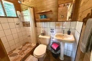 Small bathroom with shower, toilet, and sink in a jungle hotel setting.