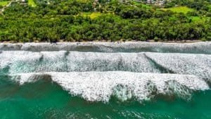 Aerial view of Costa Rica coastline with green forest, white surf, and turquoise water.