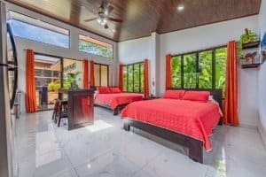 Spacious bedroom with red bedding, modern dark wood furniture, and large windows.