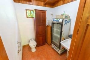 Small bathroom with toilet, mini fridge, and sink in lush jungle setting.