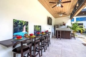Covered patio with long dining table, colorful place settings, and outdoor bar in Dominical area.