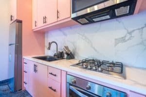 Pink kitchen with marble backsplash, stainless steel stove, and modern fixtures.