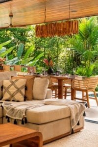 Outdoor dining area with hanging meat, tropical plants, and cushioned seating in jungle patio.