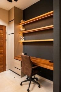 Modern home office with wooden desk, dark accent wall, and floating shelves.