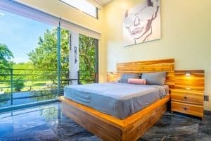 Dominical condo bedroom with wooden bed and glass balcony view.