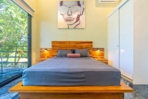 Bedroom with wooden bed frame, blue bedding, modern art above, and balcony view.