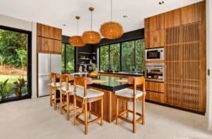Modern kitchen with wooden cabinetry, large windows, and island seating in a tropical jungle Villa.