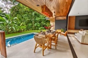 Outdoor dining area by a pool in a lush tropical garden with wooden ceiling and seating.