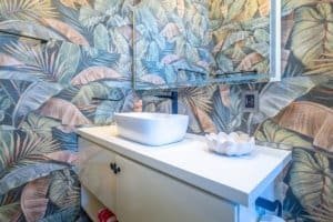 Ocean villa bathroom with palm leaf wallpaper and modern sink.
