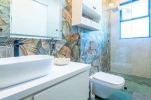 Oceanfront bathroom with tropical leaf wallpaper and modern fixtures.