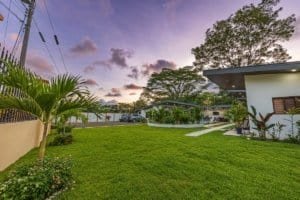 Lush green lawn with modern villa and palm plants at dusk.