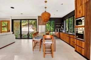 Luxury jungle home kitchen with wooden cabinets, island, and large windows.