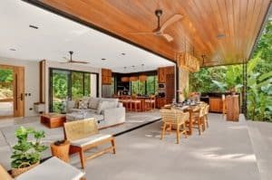 Open-plan outdoor living area with natural wood ceiling, modern kitchen, and lush greenery in Costa.
