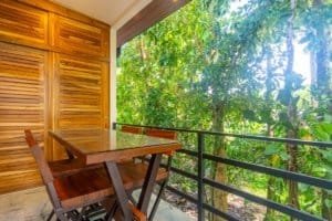 Ocean view balcony with wooden table and chairs amid tropical greenery.