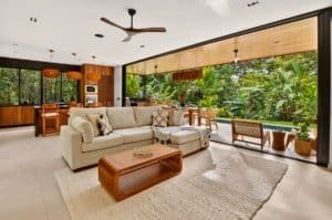 Luxurious open living space with neutral sofa, wooden coffee table, and tropical greenery outside.