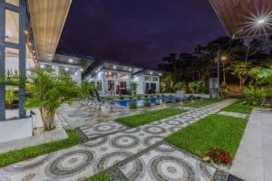 Night view of a modern villa complex with a rectangular pool and patterned stonework path.