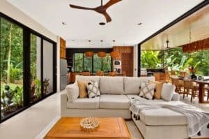 Bright open living space with cream sofa, wooden accents, and tropical garden view.