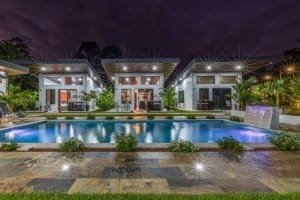 Nighttime view of a modern villa complex with a large pool and illuminated outdoor seating.