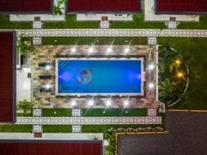 Aerial view of a rectangular swimming pool surrounded by patterned pathways and villas.