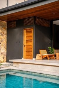 Wooden door and poolside seating at modern jungle villa entrance.