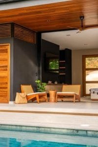 Luxurious outdoor living area with wood ceiling and poolside chairs in tropical villa.