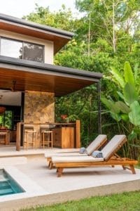 Outdoor lounge area with wooden chairs near pool and tropical garden in Costa Rica.
