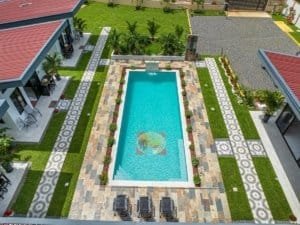 Aerial view of a modern resort-style villa with a rectangular pool and surrounding stone and green-t.