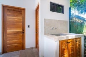 Two wooden doors beside an outdoor sink with stone countertop and green foliage.