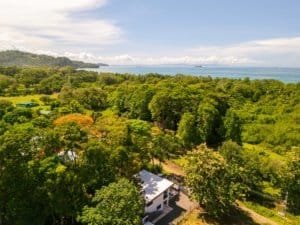 Ocean view condo in dense green trees near coastline with water in distance.