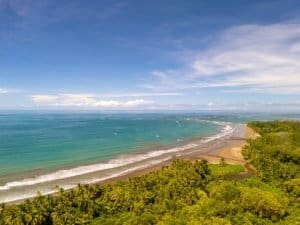 Panoramic ocean view over Dominical beach with turquoise water and palm trees.