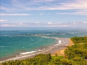 Dominical beach and turquoise sea with green hillside and blue sky.