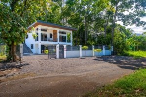 Two-story white house with a gated driveway and lush tropical trees in Costa Rica.
