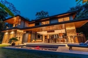 Dominical Real Estate: modern two-story villa with illuminated patio, pool, and tropical landscaping.