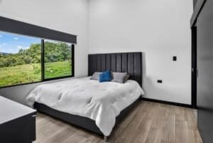 Bedroom with large window overlooking lush green landscape and mountain views.