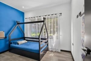 Bright bedroom with blue accent wall, house-shaped bed, and mountain views.