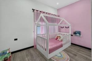 Cute children's bedroom with house-shaped bed, pink curtains, and mountain views.