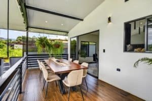 Balcony of modern home with dining table, mountain views, and outdoor seating.