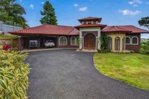 Large house with red roof, garage, and mountain scenery in Dominical.