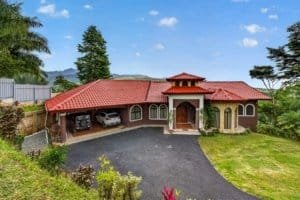 Large house in Costa Rica with red roof, surrounded by lush greenery and mountains.