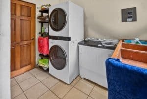 Laundry room with stacked washer and dryer, utility shelves, and laundry sink.