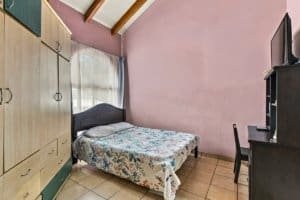 Bedroom with pink walls, wooden wardrobe, and a bed with floral bedding in Dominical.